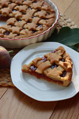 Slice of tart with dark fig jam on a white dessert plate  on wooden table with fresh figs and autumnal leaves