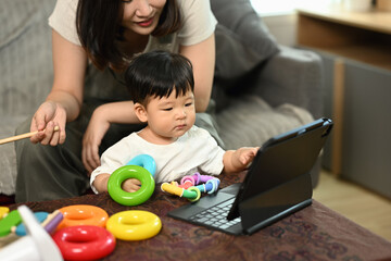 Cute little boy with mom sitting in living room looking at digital tablet screen