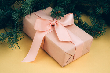 Christmas, festive background. Rose gift box with pink ribon on green coniferous branches on a yellow background. Top view