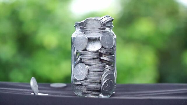 A glass container full filled with stacks of coins and some coins rained down from above and scattered. The concept of saving. Economy.