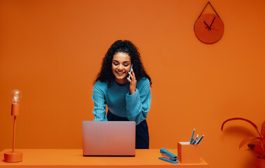 Businesswoman discussing on smartphone while working on laptop in a vibrant monochromatic office