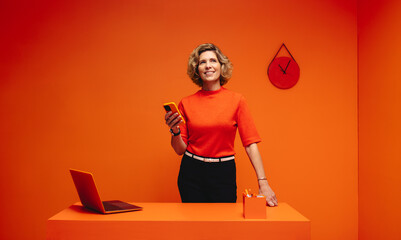 Happy woman texting on cellphone in vibrant monochromatic orange office set, emphasizing creativity and modernity