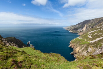 Fototapeta premium The dramatic cliffs of Slieve League in Ireland extend into the Atlantic Ocean, with grassy slopes and rocky outcrops. The expansive view highlights the clear blue water and sky