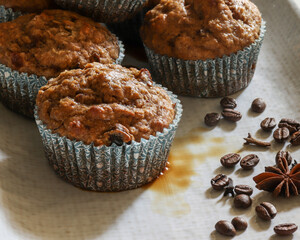 Chai spiced muffins with coffee syrup. In blue paper cupcake holders with whole star anise, cloves, coffee beans on a white plate.