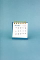 December 2025 white desk calendar on blue background.