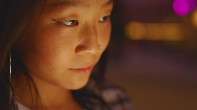 Closeup portrait of Chinese woman using phone at night. She is text messaging and thinking.