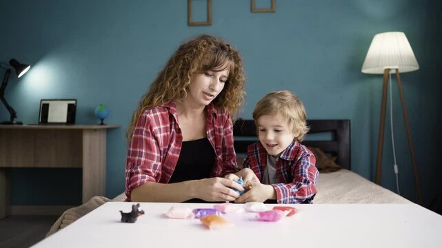 Mother with her little son unpacked plasticine. Woman and boy mold from plasticine in the living room