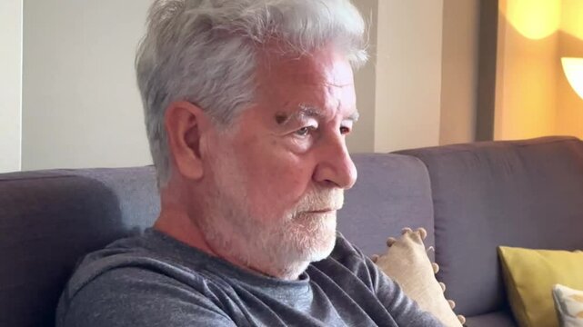A mature man sits alone on the couch, sighing with resignation and a quiet sense of sadness. His thoughts drift between memories and the passing of time, evoking a sense of isolation and reflection