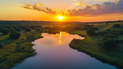 Aerial view of a lake reflecting a stunning sunset with green hills and trees surrounding it.