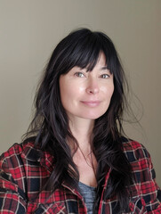 Fototapeta premium Portrait of a young woman with long black hair wearing a plaid shirt, standing against a gray background. Concept of casual fashion and natural beauty