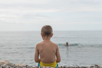 Sad child sitting alone on rocky beach by the sea