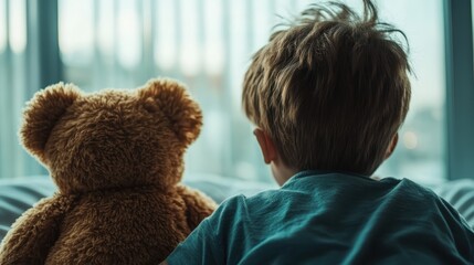 A little boy sits side by side with a plush bear perched next to him, gazing out a window in the morning light, evoking curiosity and companionship.