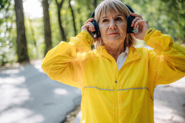Positive facial expression. Senior woman in yellow sport coat is outdoors with headphones