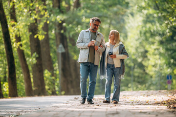 Obraz premium Coffee cups in hands, walking around. Senior couple together outdoors at nature
