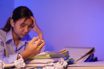 A young woman works overtime at night at her desk in office, using a laptop reviewing documents. is stressed, tired,experiencing headaches,body aches from sitting too long,leading to office syndrome