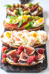 Open sandwiches with avocado and salmon, sun-dried tomatoes and olives, crabs with egg, figs with berries.