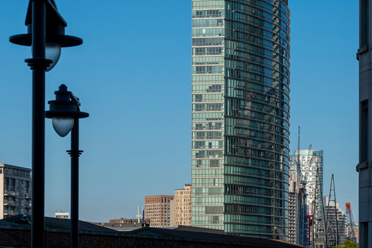 The image focuses on a tall skyscraper rising into a clear blue sky, set in an urban skyline that features a blend of modern and classic architectural designs in London