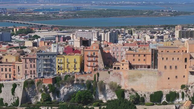 Aerial view of Cagliari, Italy, featuring the Castello district, Cagliari Cathedral, Gulf of Cagliari, salt flats, and wind turbines.