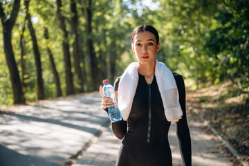 Stay hydrated, with bottle of water, standing. Young sportive skinny woman is in black fitness...