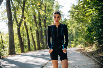 Obraz premium Young sportive skinny woman is in black fitness clothes outdoors