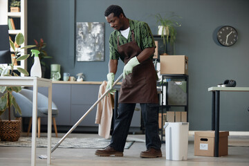 Full length side view of adult African American man mopping floors in office and enjoying Spring cleaning at workplace, copy space