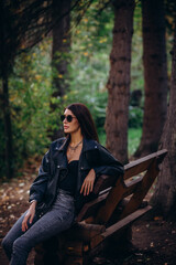 Woman, an adult and a beautiful brunette in a leather jacket and jeans, walks in the park in autumn.