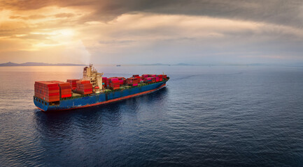 Aerial view of a large, loaded container cargo ship sailing over calm sea into the sunset with copy...