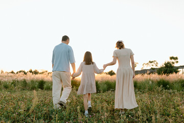 Happy family with child holding hands of each other and running through wheat field at sunset enjoying nature together