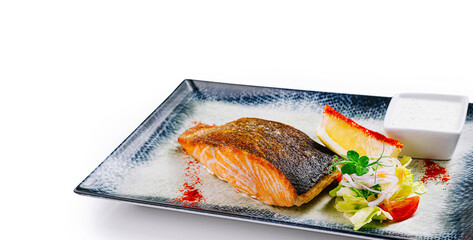Grilled salmon steak with vegetables and white sauce on elegant restaurant plate