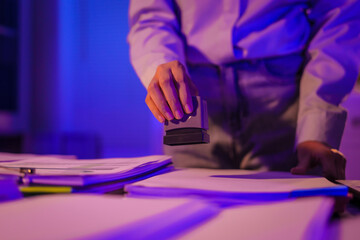 young Asian business trainee works late into night at her desk, by papers and a laptop. Exhausted and stressed, she battles fatigue and headaches as deadlines loom, feeling overwhelmed.