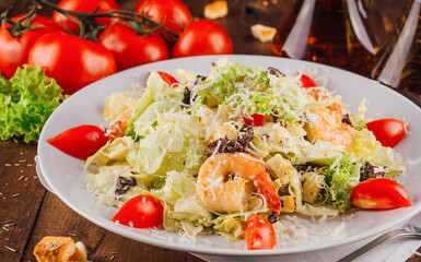 Delicious caesar salad with shrimps on white plate being served on wooden table