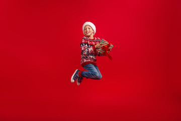 Full size photo of cute little boy jump look empty space hold gift celebrate new year wear knitted...