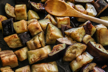 A frying pan with sautéed eggplant and a wooden spoon.
