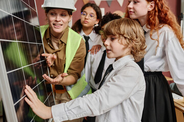 Caucasian teen boy asking questions about solar energy while touching cell panel surface during...