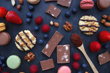 Macarons, chocolate, cookies, berries and various nuts on dark blue background. Top view.