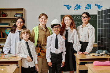 Group of young teacher, female engineer and gen alpha students posing for portrait in classroom on...