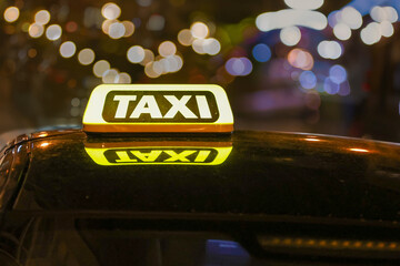 Close-up view of a brightly illuminated yellow taxi sign on the roof of a vehicle.