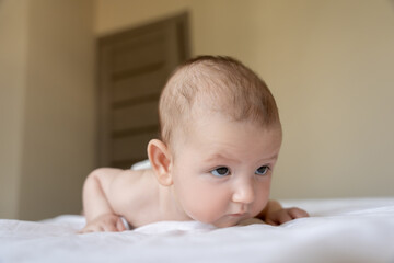 Infant baby girl or boy lying on his belly on bed looking away