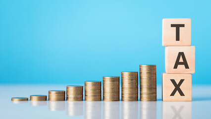 TAX is write on a wooden block next to a stack of coins. Against light blue background. Tax awareness, financial planning, savings, and effective money management