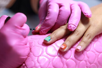 Nail technician applying detailed nail art design with bright colors, wearing pink gloves during a professional manicure session. Manicure concept