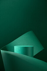 A single green cylinder podium with a green backdrop and a green paper ribbon winding around it...