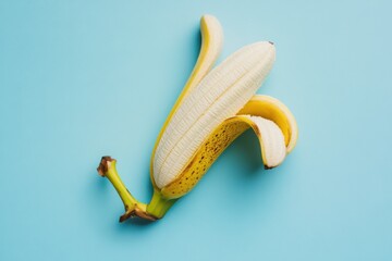 A partially peeled banana resting on a light blue surface, showcasing its vibrant yellow color