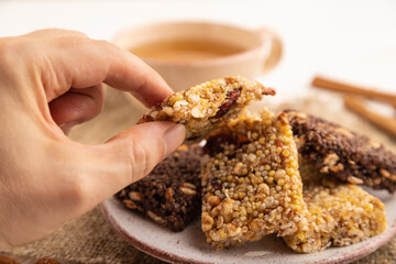 Granola bars with caramel, nuts, flakes in ceramic plate with hand on white wooden. Side view, selective focus.