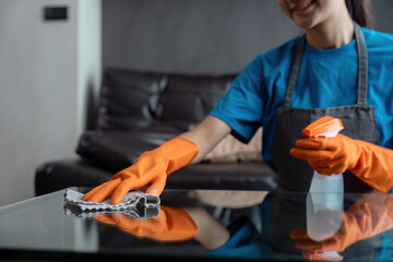 Professional Housekeeper Cleaning Glass Table with Orange Gloves and Spray Bottle in Modern Living Room