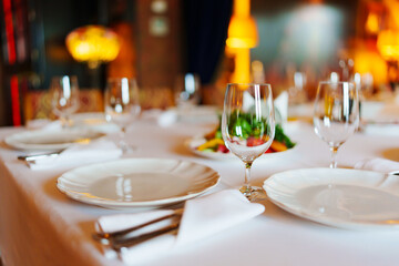 An empty wine glass and plates on a table served for a banquet. 
