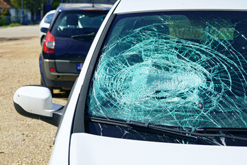 A white passenger car with a broken windshield parked on the side of the road. The aftermath of a...