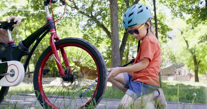 Boy wearing blue helmet carefully inflates bicycle tire on pathway. Preschooler kid independently pumps flat bicycle tire to keep riding safely