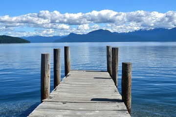 Serene wooden dock extending over calm waters under a bright blue sky with fluffy clouds