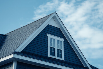 Close-Up of a Classic Suburban House Roof with White Trim and Blue Siding Against a Clear Sky