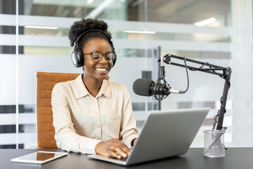 Smiling woman recording podcast in modern office with laptop, microphone, headphones. Engaged in...